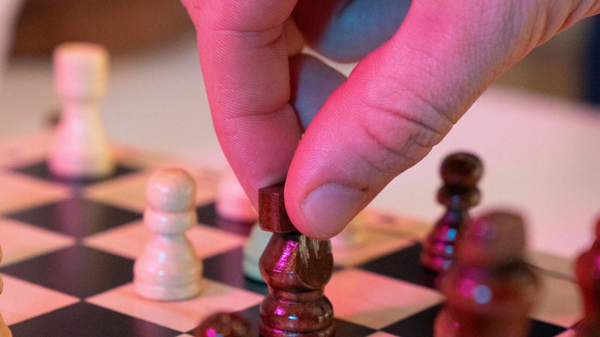 A hand strategically moves a chess piece on a board, focusing on strategy and concentration.